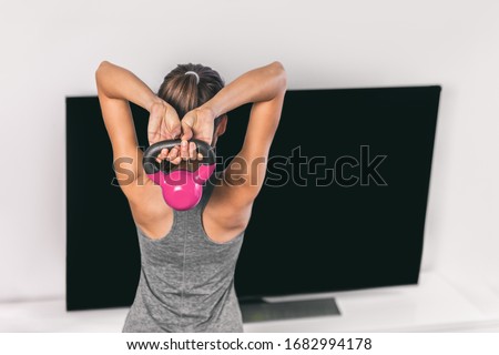 Home strength training workout overhead triceps extension muscles exercises woman watching online tv class live streaming at home. Fitness gym girl lifting kettlebell weights.