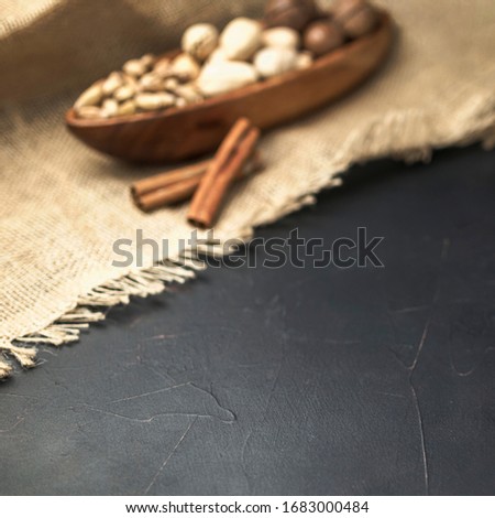 nuts in a wooden bowl shaped like a boat on a dark concrete background and burlap