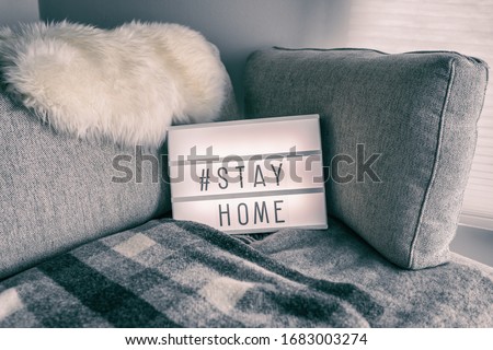 Coronavirus home lightbox sign with hashtag message #STAYHOME glowing on home sofa with cozy lambswool fur, blanket. COVID-19 text to promote self isolation staying at home.