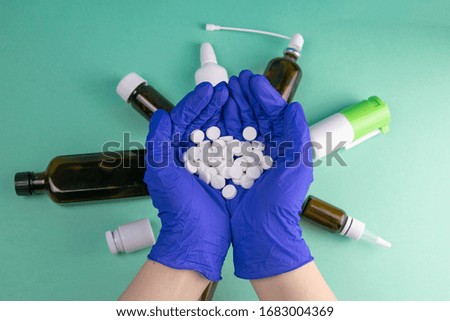Many small white pill in the doctor's hands dressed in the medical blue disposable gloves.