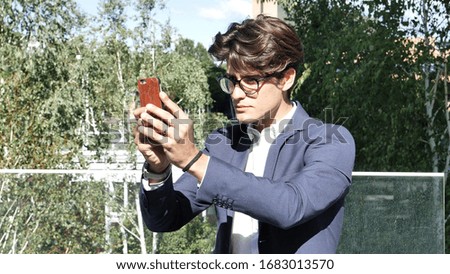 Handsome young man in city setting, taking photos with cell phone