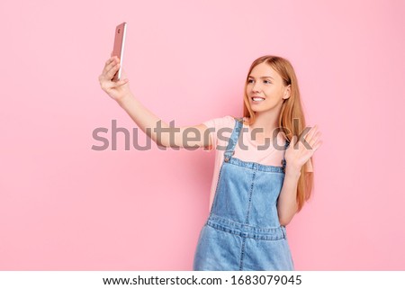 An attractive young stylish woman takes a selfie on her smartphone on an isolated pink background