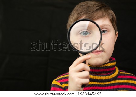 Little short haircut girl looks through a magnifier into the screen. Studio photo on a black isolated background.