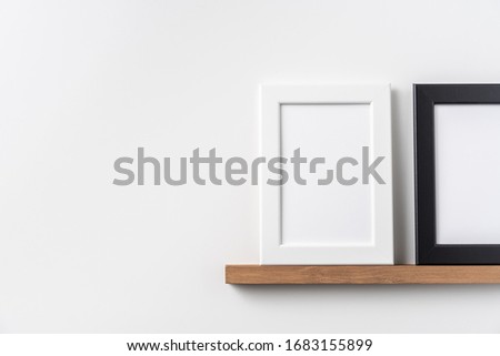 Design concept - front view of vertical white and black wood photo frame on bookshelf and white wall for mockup