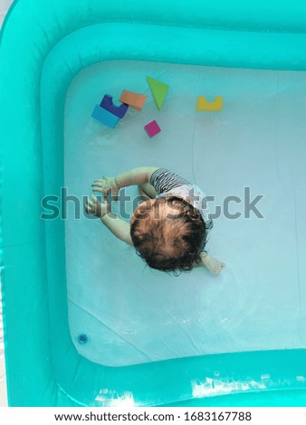 A toddler was playing in the inflatable pool. Selectively focused and partially pool in frame. 