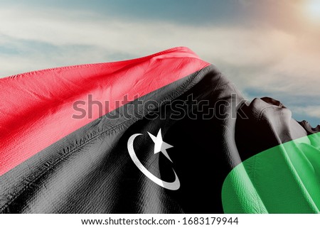 Libya national flag cloth fabric waving on beautiful sky.