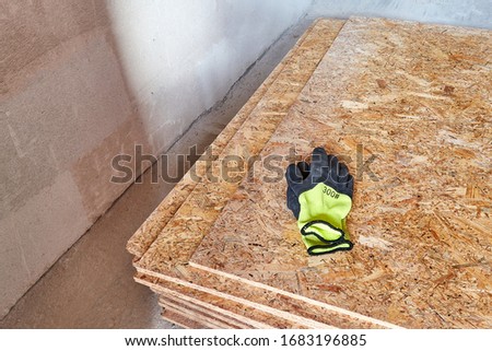OSB slab building material made from reborn sawdust. They lie in a pile, yellow protective gloves lie on it. Close-up.