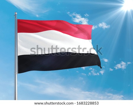 Yemen national flag waving in the wind against deep blue sky. High quality fabric. International relations concept.