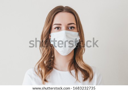 Portrait of a young girl in a medical mask isolated on a white wall background. Young woman patient, copy space Royalty-Free Stock Photo #1683232735
