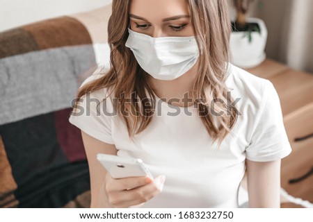 A woman sits on the bed in her room in quarantine isolation, holds a cell phone and reads news about the coronovirus. Young girl working remotely at home, quarantine concept. Call to the ambulance