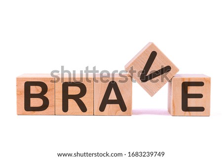 Word BRAVE is made of wooden building blocks lying on the table and on a light background.