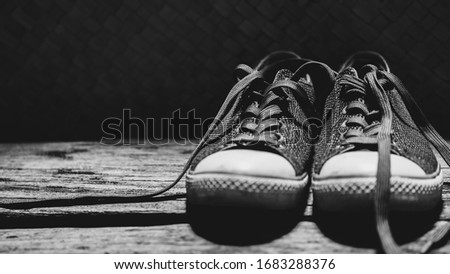 Sneakers with grey shoelaces on vintage wood plank against dark background with copy space. Black and white photography design.