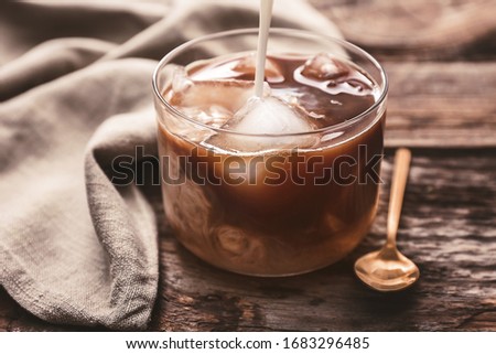 Pouring of milk in glass of tasty iced coffee on table