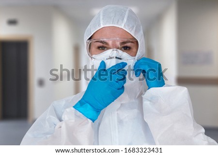 Women doctor wearing  protective suit to fight coronavirus pandemic covid-2019. Protective suit, googles, gloves, respirator. Royalty-Free Stock Photo #1683323431