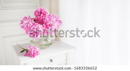 Pink peonies in glass vase. Flowers on white table near the window. Morning light in the room. Beautiful peony flower for catalog or online store. Floral shop and delivery concept. Banner. Copy space