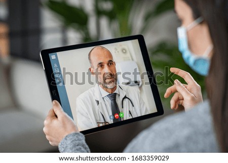 Sick woman wearing protective mask during video call with mature doctor. Back view of patient with surgical face mask talking during conference call with her physician, staying at home in quarantine.  Royalty-Free Stock Photo #1683359029