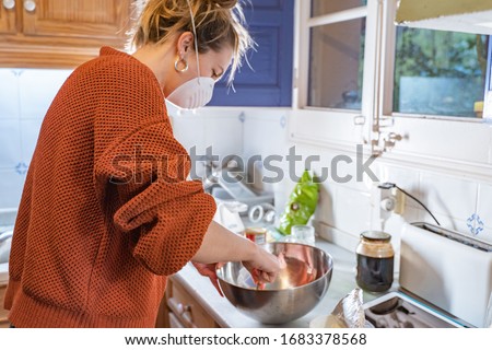 Coronavirus. Woman with face mask on quarantine, cooks in the kitchen at home during coronavirus crisis. Stay at home. Enjoy cooking at home. Family concept.