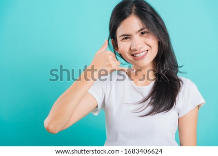 Portrait Asian beautiful happy young woman wear white t-shirt standing smile white teeth, making call me gesture on a blue background, with copy space
