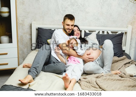 Happy father, daughter and pregnant mother have cuddles in bed, wearing home pijamas in bedroom.