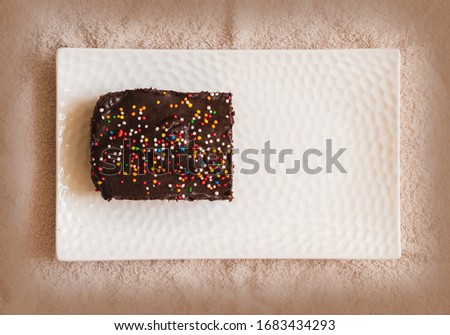Cocoa cake with chocolate flavored icing and colorful sprinkles, placed on a white porcelain tray