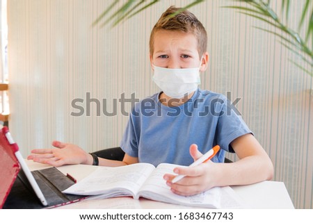 10-year-old boy schoolboy does distance learning lessons on a tablet while sitting at a table in a mask, the topic of distance learning of students in quarantine