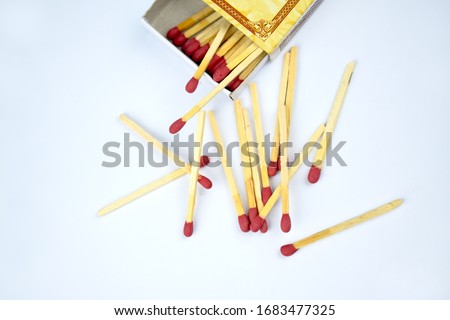 Top view picture of some flammable red fire matches scattered beside a small match box before a white background