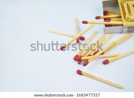 Close up picture of some flammable red fire matches scattered beside a small match box before a white background