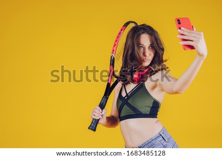 A young and friendly lady, well-disposed, with a smile and sporty dress, makes selfies and holds in your hand a tennis racket.
