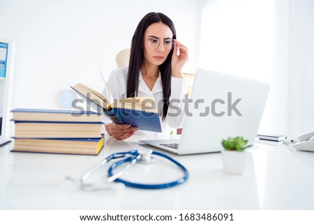 Photo of pretty professional doc lady hold science literature attentively reading symptoms of rare disease look notebook wear specs white lab coat sit chair office clinic indoors
