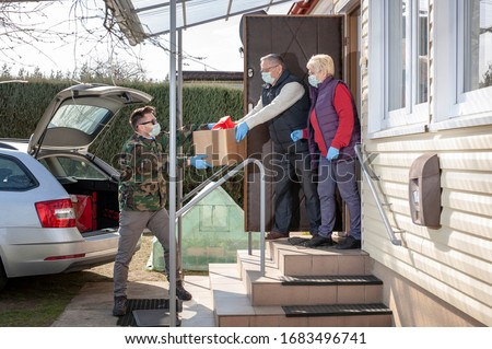 coronavirus pandemic. Epidemic. A volunteer / soldier brought food for senior citizens. On the steps, a volunteer in a medical mask and gloves passes a bag of products to an elderly couple in masks Royalty-Free Stock Photo #1683496741