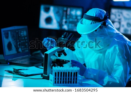Scientist in protection suit and masks working in research lab using laboratory equipment: microscopes, test tubes. Coronavirus 2019-ncov hazard, pharmaceutical discovery, bacteriology and virology. Royalty-Free Stock Photo #1683504295