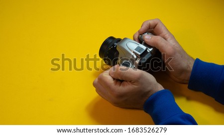 
Hands of a man with a photo camera on a yellow background