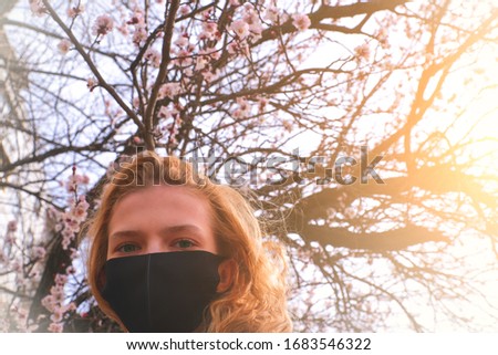 Girl in a medical mask on a background of flowering trees. The mask is black. Protection against virus, flu. Spring allergy