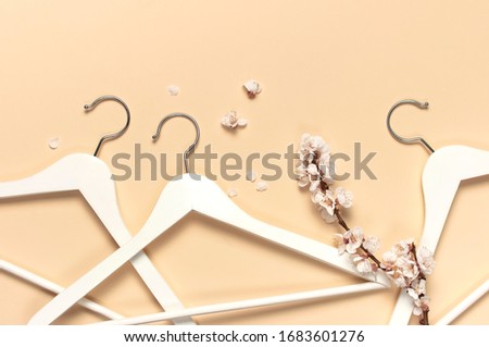 Creative spring sale concept. White wooden hangers with spring sprigs of apricot flowers on beige background top view flat lay. Fashion spring discounts shopping sale store promo design minimalism 