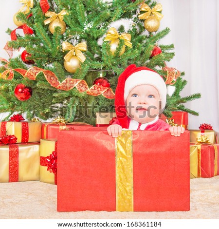 Happy smiling child in christmas hat in gift box against decorated fir tree