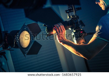 Caucasian Video Camera Operator in His 30s Taking Apartment Interior Shoots Using Blue and Orange Artificial Lighting.