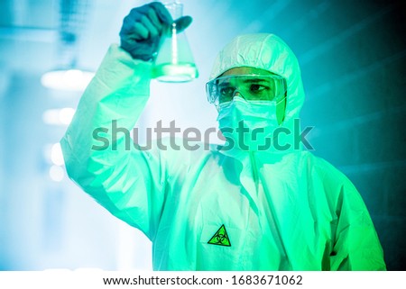 corona virus concept. male scientist doctor in mask, glasses and protective suit reviewing glass flask with green liquid