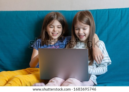 Two happy children are sitting on the couch and watching cartoons on a laptop, playing games, studying online with distance learning, e-learning concept