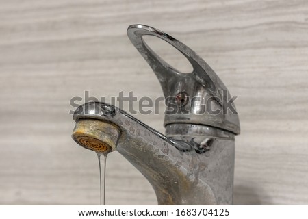 A thin stream of hard water flows from an old tap aerator. Old Bathroom Sink Faucet contaminated with calcium and grime. Royalty-Free Stock Photo #1683704125