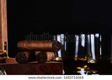 Still life with three cuban cigars, two glasses of whiskey or rum and wooden box with hygrometer and black background. Space for your text. Royalty-Free Stock Photo #1683716068