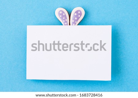 Easter background concept. Easter bunny ears under white empty paper on blue background.