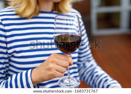 Girl in a striped vest holds a glass of red wine.