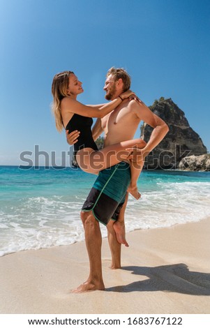 Young happy couple on an azure ocean background. The girl in the arms of a guy hugs him. A guy and a girl are hugging on the beach of the island Nusa Penida, Indonesia