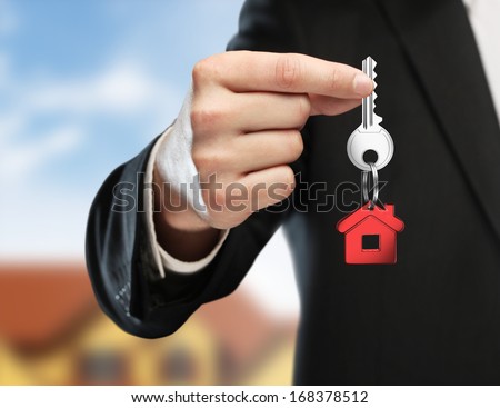 hand handing key on cottage background Royalty-Free Stock Photo #168378512