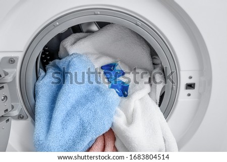 Person putting detergent pods in washing machine with laundry