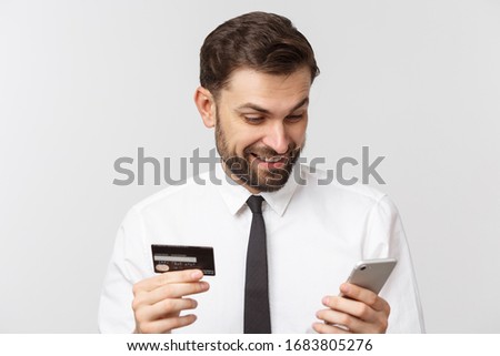 Photo of confident entrepreneur man in suit and tie holding smartphone and credit card for paying online isolated over gray background.