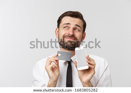 Photo of confident entrepreneur man in suit and tie holding smartphone and credit card for paying online isolated over gray background.