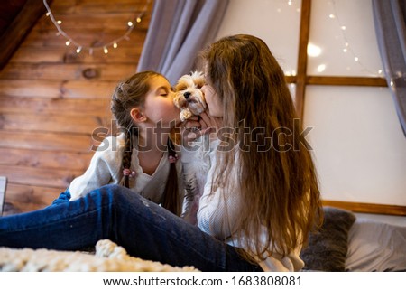 mom and daughter kiss their pet dog sitting on the bed in the bedroom