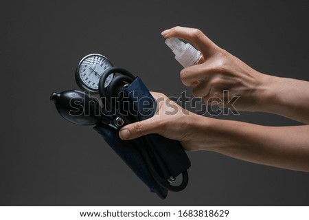Lady hand applying alcohol spray hand sanitizer towards the Sphygmomanometer to prevent the spread of bacteria and virus. Personal hygiene concept. Isolated black background