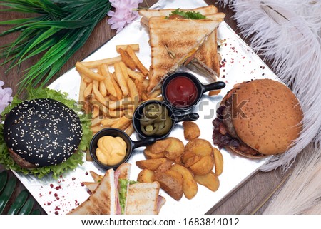 Big black hamburgers, French fries, sauces and vegetables